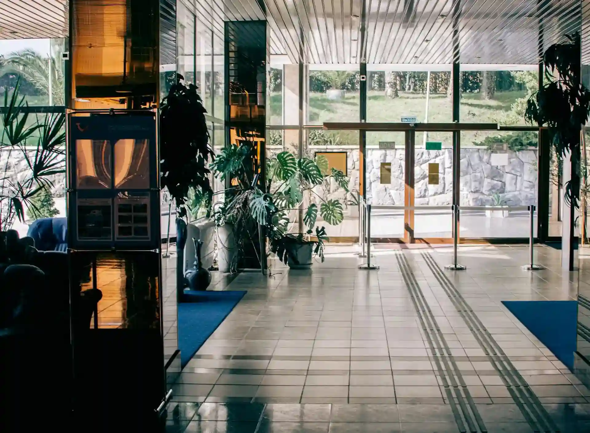 Well lit hotel lobby with stone floors, blue carpets, big windows and lots of plants.